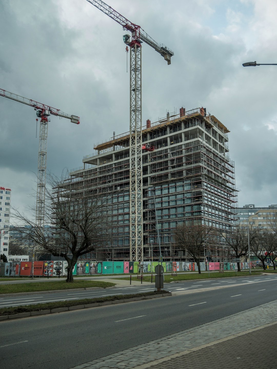 Tower cranes loom over a concrete building under construction.